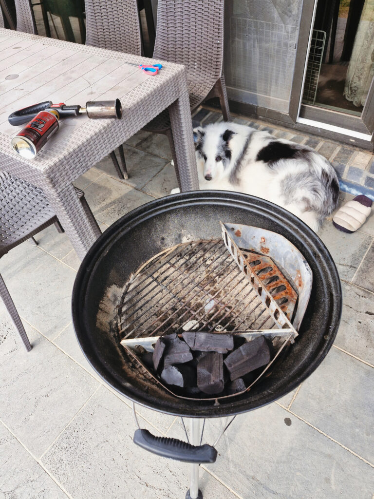 마당 데크 위 웨버 그릴에서 가스 토치로 바비큐 숯불을 피우는 모습