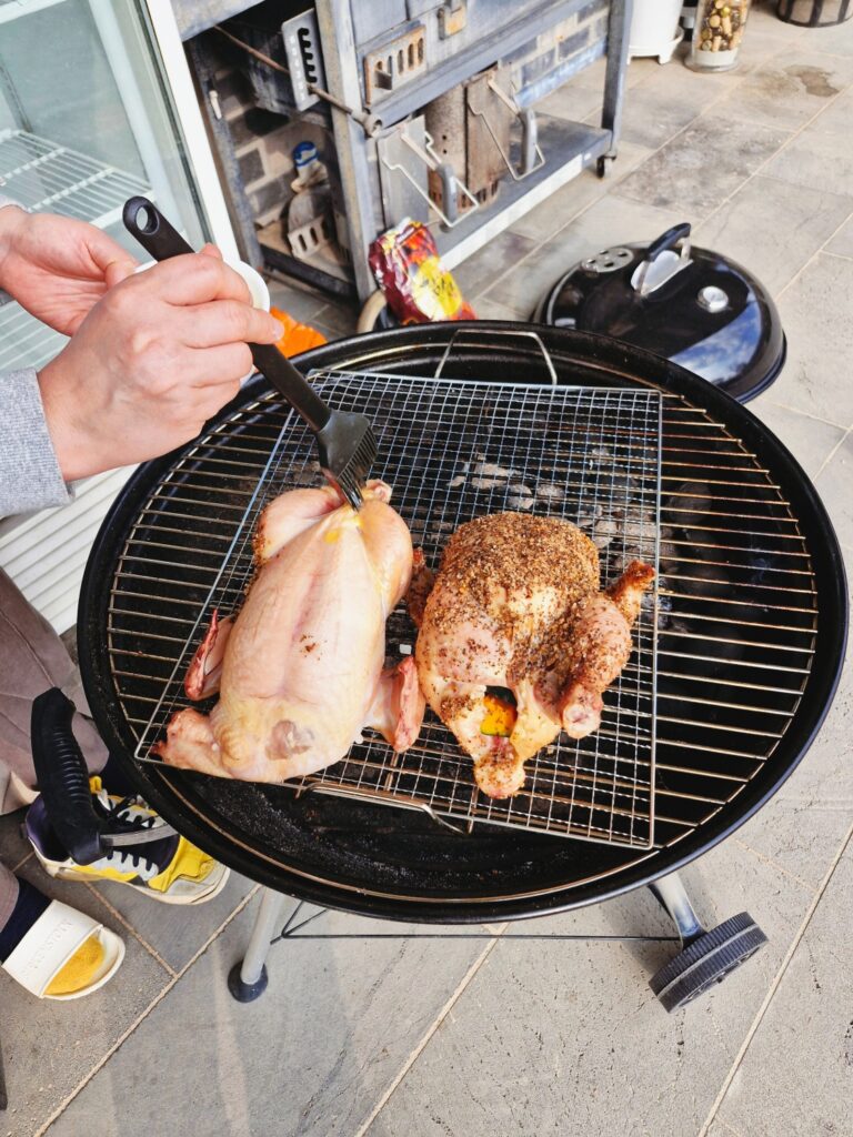 A hand brushing melted butter onto a whole chicken on a Weber grill