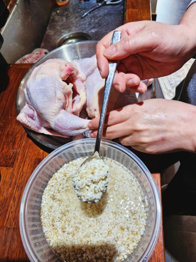 A person stuffing raw rice into a whole chicken using a spoon (Close-up)