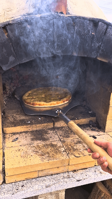 Taking out a freshly baked, crispy wood-fired pizza from the brick oven