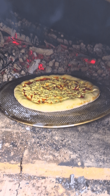 Wood-fired pizza baking inside a hot brick oven with melting cheese and bubbling crust