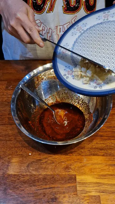 Adding the prepared crushed garlic into the mixing bowl with all seasonings
