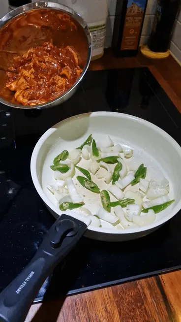Transferring the marinated Jeyuk pork over the sautéed onions and chilies in the wok