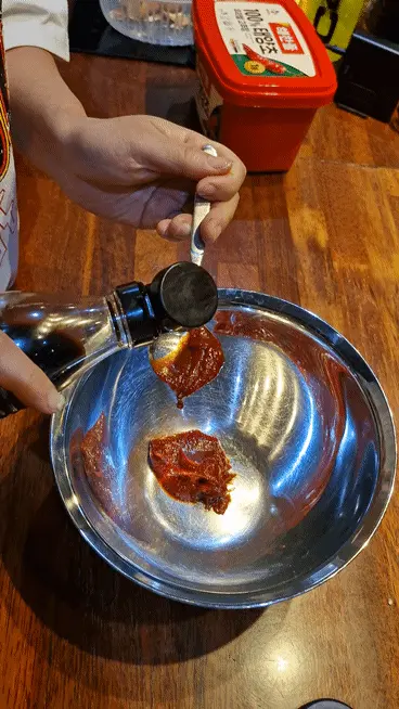 Pouring soy sauce from a bottle into the mixing bowl with Gochujang