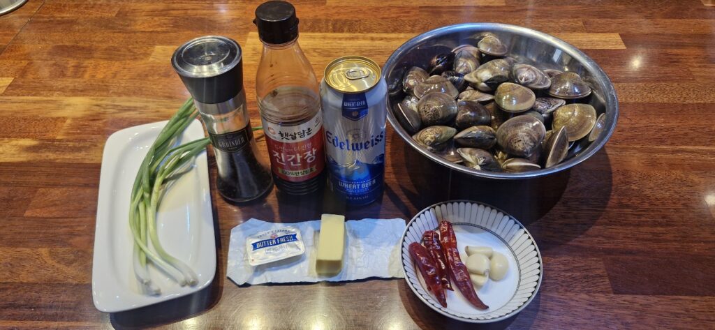 Fresh white clams, butter, garlic, red chilies, and a bottle of beer prepared on a kitchen counter.