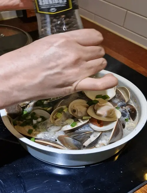 Sprinkling black pepper over the steamed clams as a final touch.