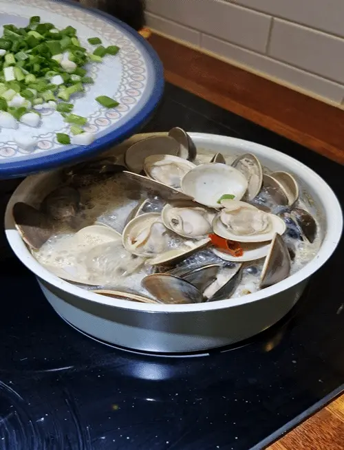 Opening the lid to reveal steamed clams fully opened in a savory broth.